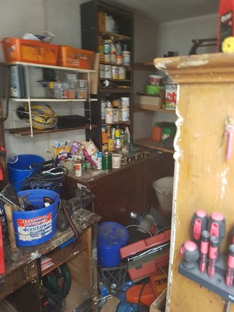 Unordentliche Werkstatt mit Regalen, Werkzeug, Farben, Schraubenziehern und Eimern.