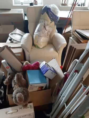 Wohnzimmer mit Umzugskartons, Sessel, Kartons und Haushaltsgegenständen beim Umzug.