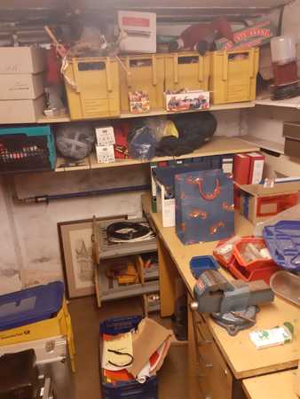 Unordentlicher Kellerraum mit Regalen, Werkzeugen, Kisten, Ordnern und Bastelmaterial.